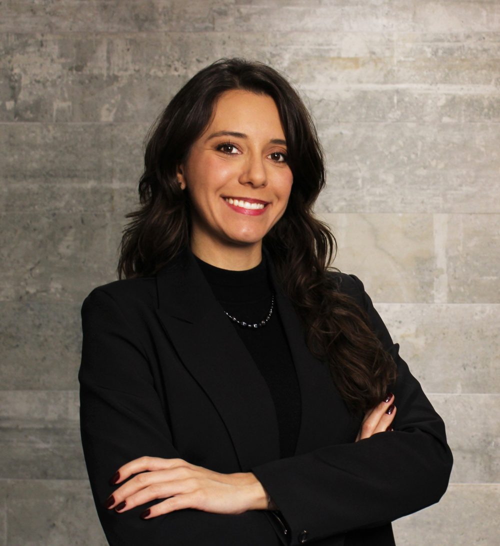 Bárbara Chelski, sorrindo, de braços cruzados, com blazer preto